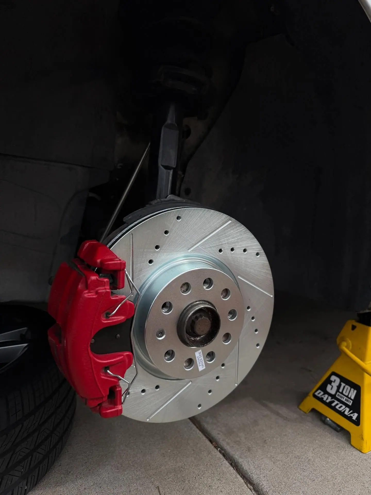 A new drilled and slotted brake rotor with a red caliper, fitted on location